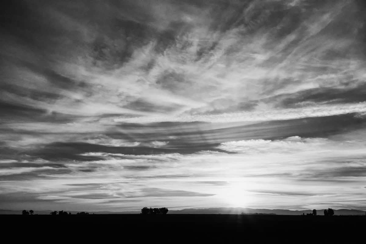 A black and white landscape image with dramatic clouds and sun rays.
